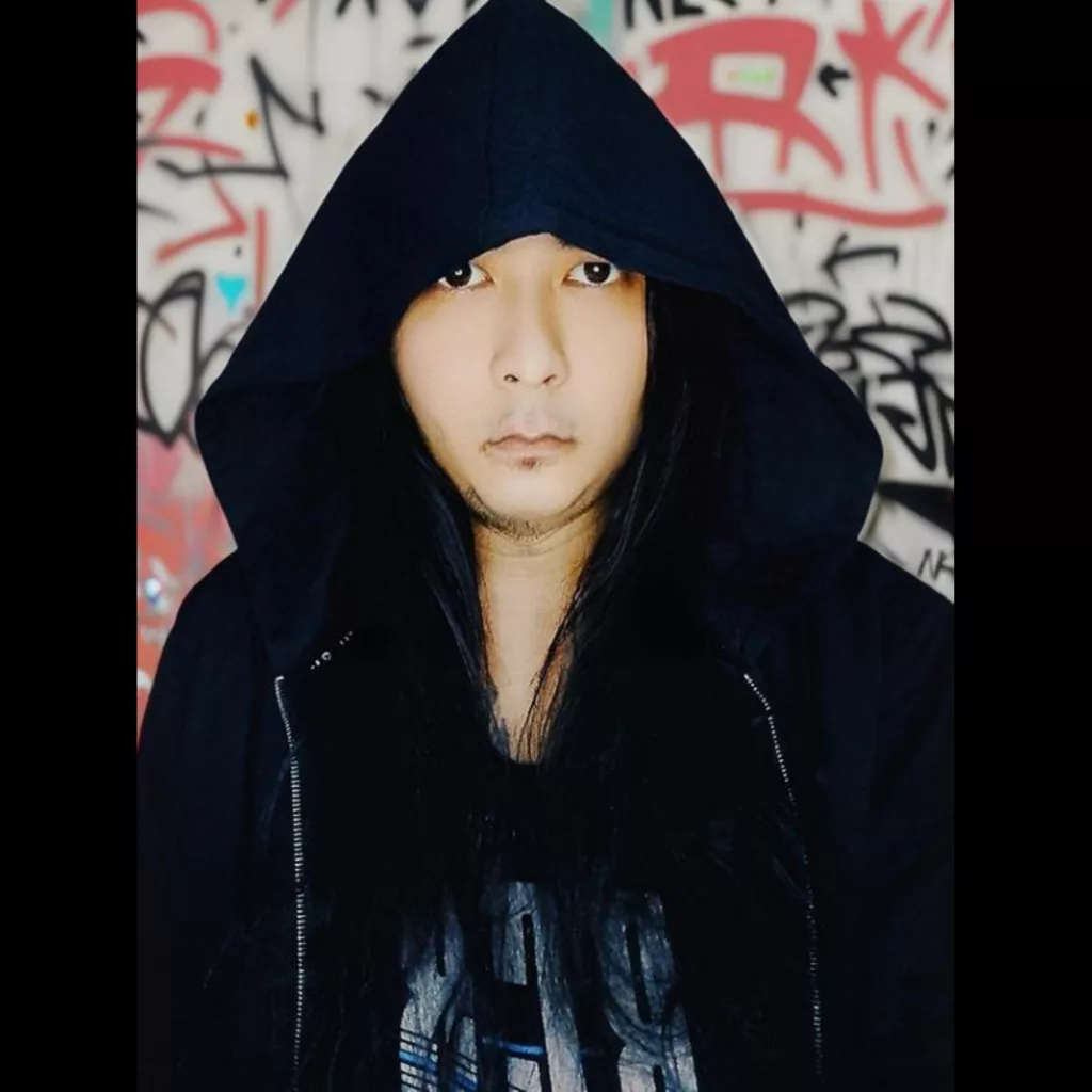 Sai Ye Htet Kaung wearing a black hoodie, standing against a graffiti-covered wall with an intense gaze.