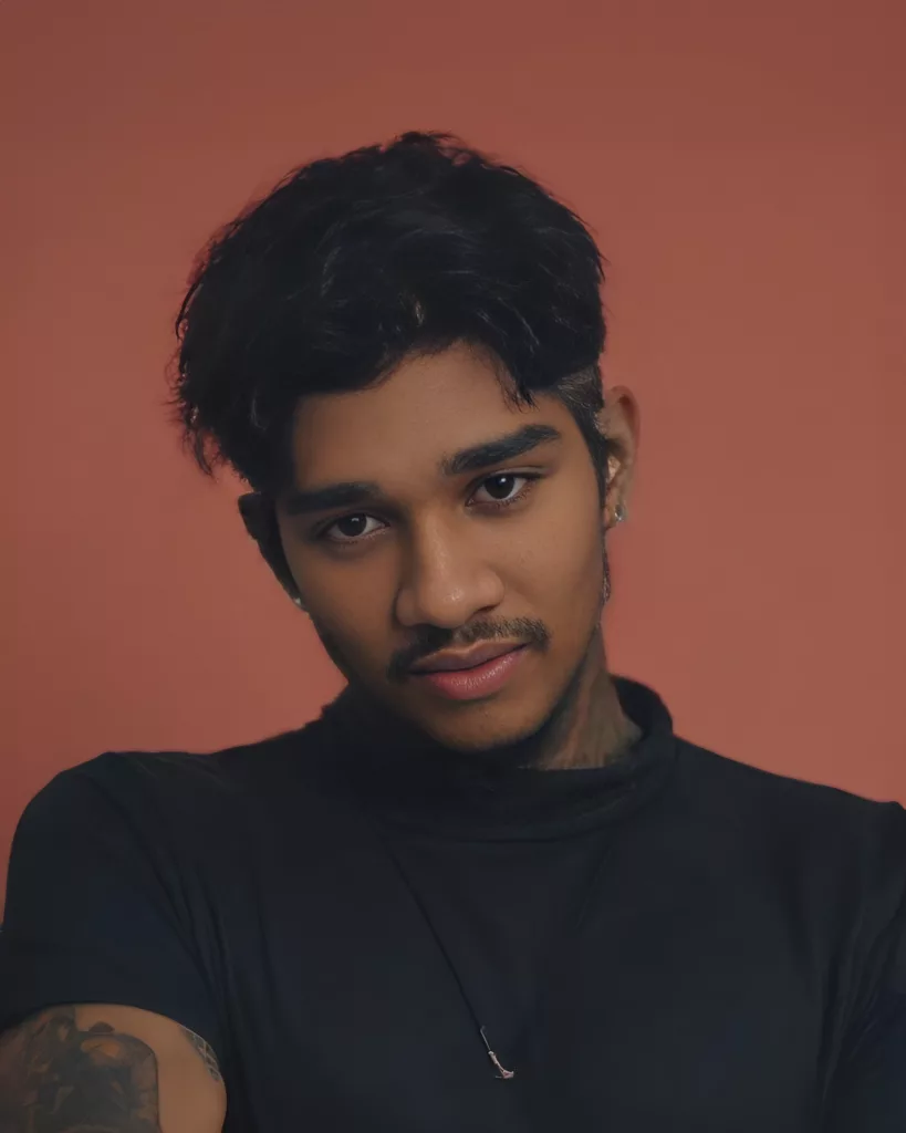 A confident portrait of Adithyakiran PB wearing a black shirt against a warm orange background.