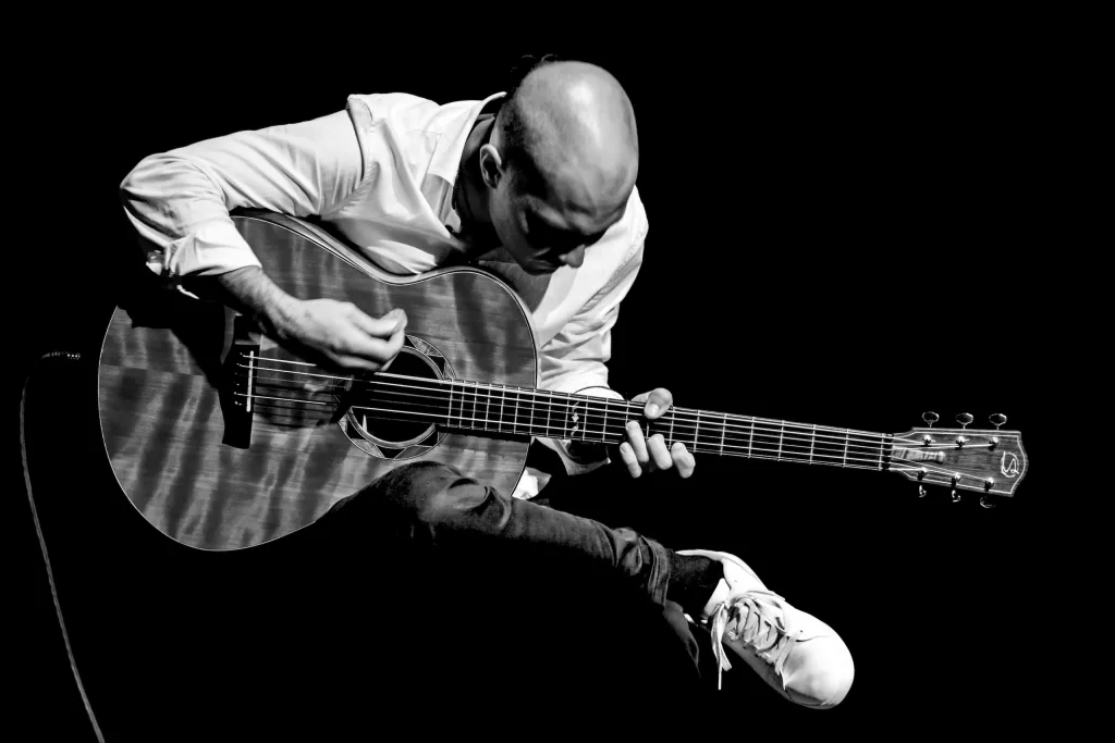 Piotr Krępeć passionately playing an acoustic guitar with an intense, focused expression.