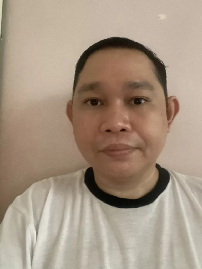 A portrait of VeeJay Lao, a singer-songwriter from the Philippines, wearing a white t-shirt with a black collar, standing in front of a light pink background.